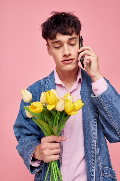 Chico joven en una chaqueta de mezclilla con un ramo de flores hablando por teléfono fondo rosa