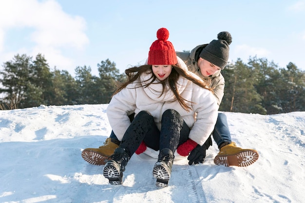 Un chico joven y una chica se deslizan por el tobogán de nieve contra el fondo del bosque y el cielo azul