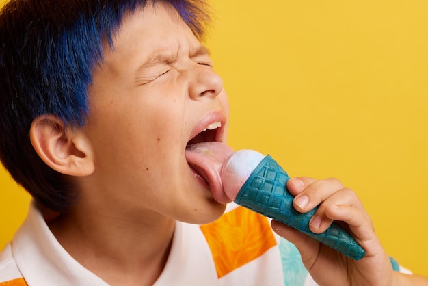 Chico joven comiendo helado apetitoso en un palo sobre un fondo amarillo