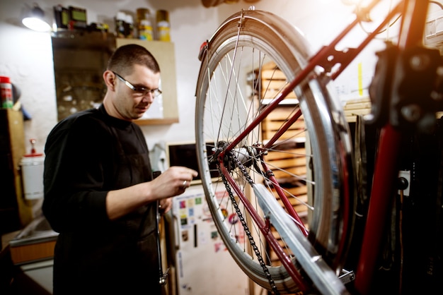 Foto chico joven comprobación de equilibrio de la rueda de bicicleta en el garaje.