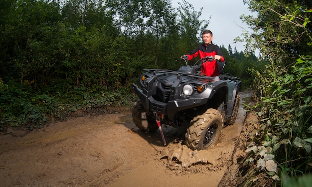 Chico joven conduciendo un vehículo todo terreno ATV a través de barro