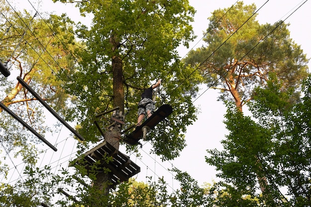 Chico joven corre una carrera de obstáculos de árbol en árbol en un parque de cuerdas