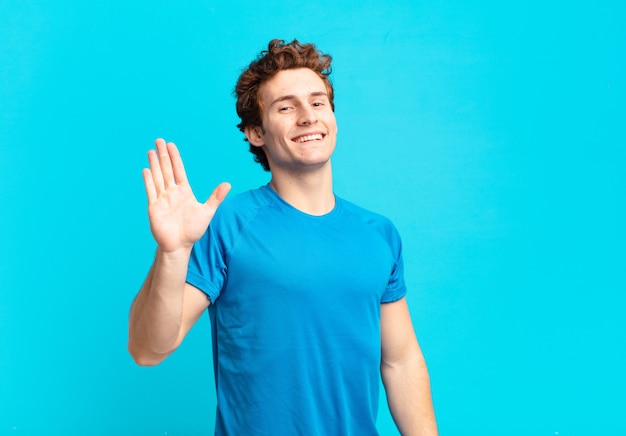 Chico joven deporte sonriendo feliz y alegremente, saludando con la mano, dándote la bienvenida y saludándote, o diciéndote adiós