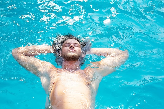 UN CHICO JOVEN ESTÁ ACOSTADO DE ESPALDA EN EL AGUA EN LA PISCINA DISFRUTA DEL CALOR Y DESCANSA