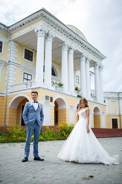 Chico joven con estilo en un traje el novio y la novia hermosa chica con un vestido blanco con un tren a pie en el parque el día de su boda