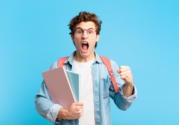 Chico joven estudiante gritando agresivamente con una expresión de enojo o con los puños cerrados celebrando el éxito