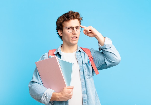 Chico joven estudiante que se siente confundido y desconcertado, mostrando que estás loco, loco o loco