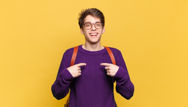 Chico joven estudiante que se siente feliz sorprendido y orgulloso apuntando a sí mismo con una mirada de asombro emocionado