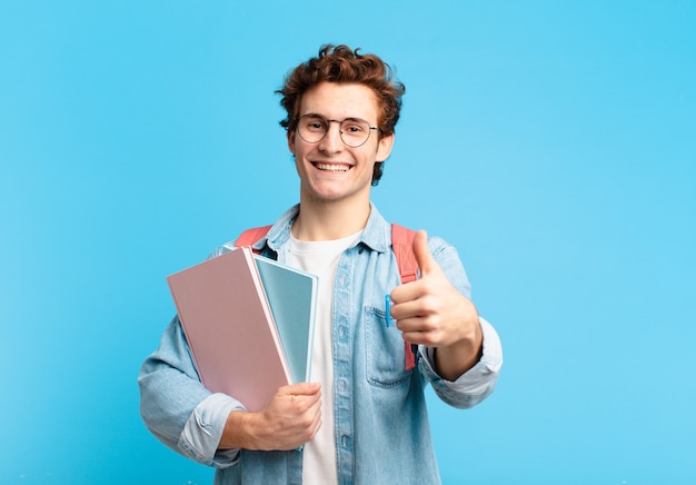 Chico joven estudiante que se siente orgulloso, despreocupado, seguro y feliz, sonriendo positivamente con los pulgares hacia arriba