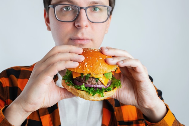 Un chico joven con gafas sosteniendo una hamburguesa fresca.