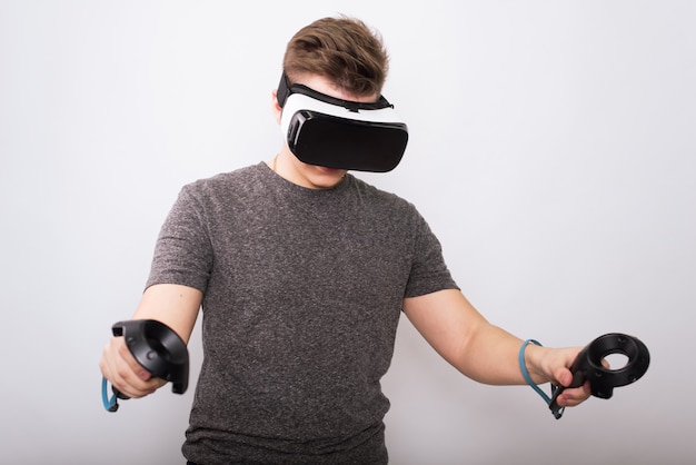 Chico joven en gafas viar. Un adolescente juega con gafas de realidad virtual y considera joysticks y gamepads