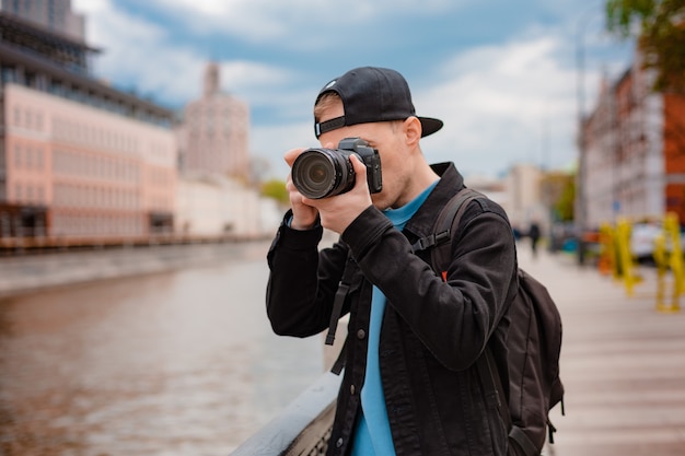 Chico joven gorra negra, hombre con cámara centro ciudad metrópolis toma fotografías. Capture momentos de vacaciones mientras viaja, fotógrafo que toma fotos con enfoque selectivo