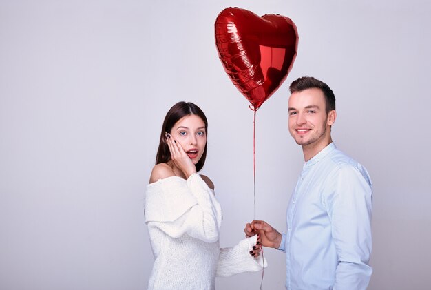 Chico joven guapo da un globo de corazón rojo.