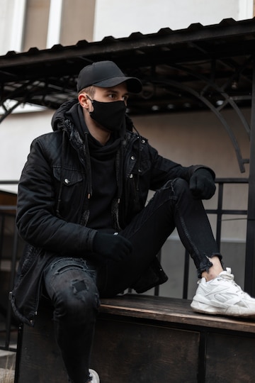 Niño unidad de repuesto Chico joven guapo con estilo con una máscara protectora médica y gorra  negra en ropa de moda con una chaqueta y una sudadera con capucha en la  calle. moda y estilo urbano