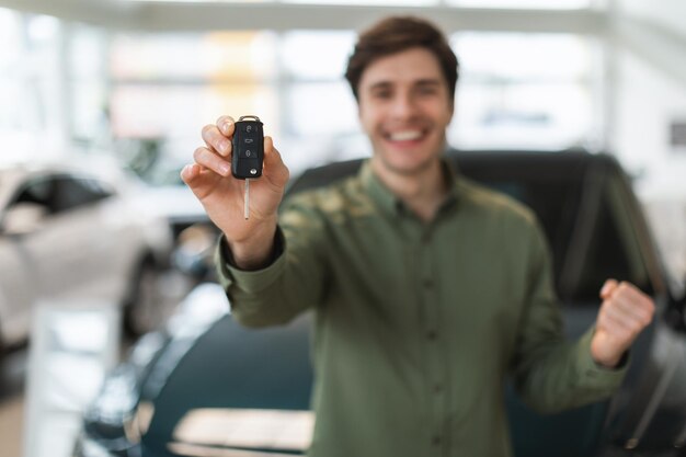 Chico joven guapo mostrando la llave del auto nuevo en la cámara haciendo un gesto de sí celebrando la compra del auto en