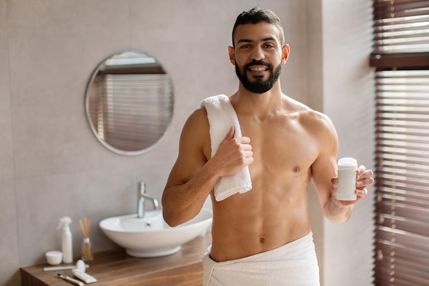 Chico joven guapo de pie con una botella de desodorante en la mano