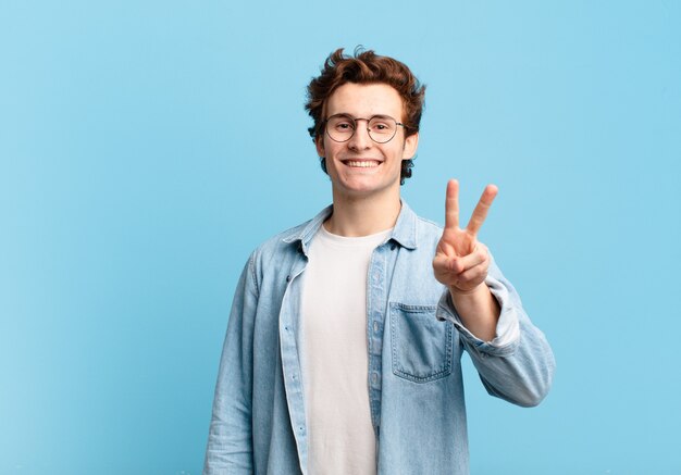 Chico joven guapo sonriendo y luciendo feliz, despreocupado y positivo, gesticulando victoria o paz con una mano