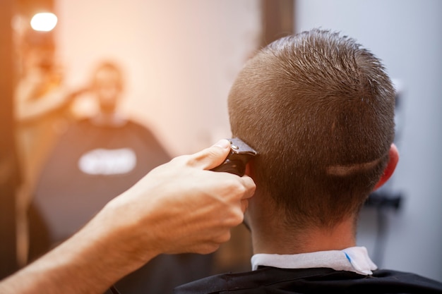 Chico joven hace un corte de pelo corto en una barbería con una recortadora, primer plano