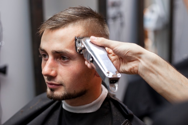 Chico joven hace un corte de pelo corto en una barbería con una recortadora