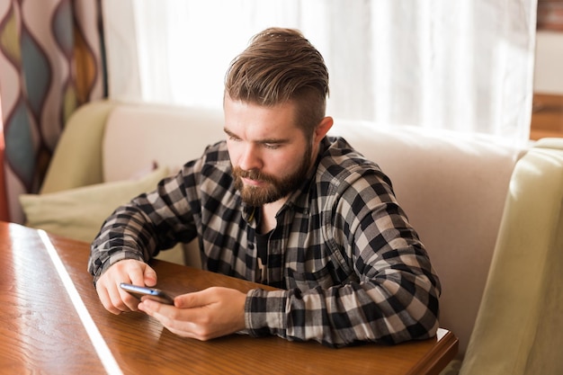 Chico joven hipster que busca noticias de las redes sociales leídas a través de un teléfono inteligente en el tiempo libre en el café