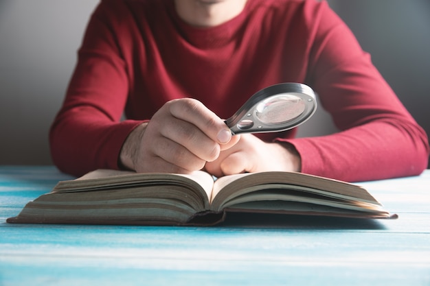 Chico joven leyendo un libro con una lupa sobre la mesa