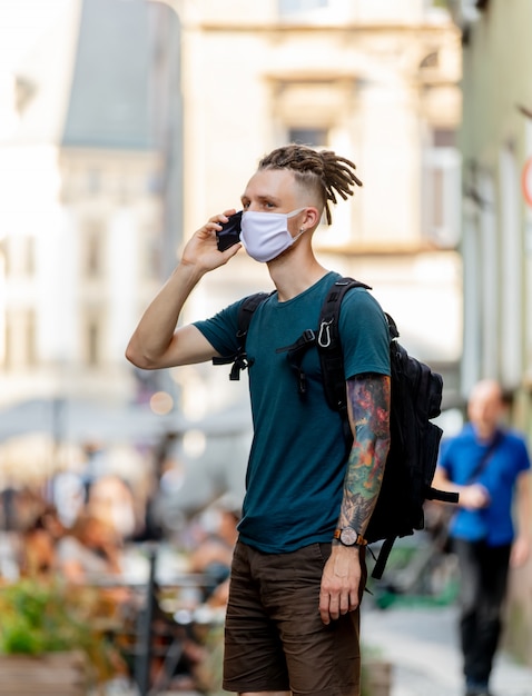 Foto chico joven con mascarilla y rastas está hablando por teléfono móvil en la calle