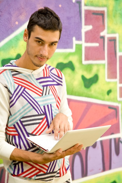 Chico joven con portátil junto a la pared de graffiti.