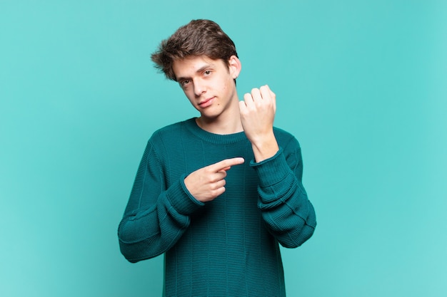 Chico joven que parece impaciente y enojado, señalando el reloj, pidiendo puntualidad, quiere llegar a tiempo