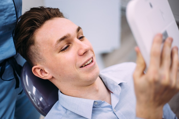 Chico joven sonríe, mira los dientes después del tratamiento en el dentista