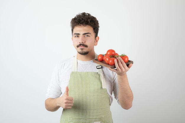 Chico joven sosteniendo un montón de tomates frescos y gesticulando con el pulgar hacia arriba.