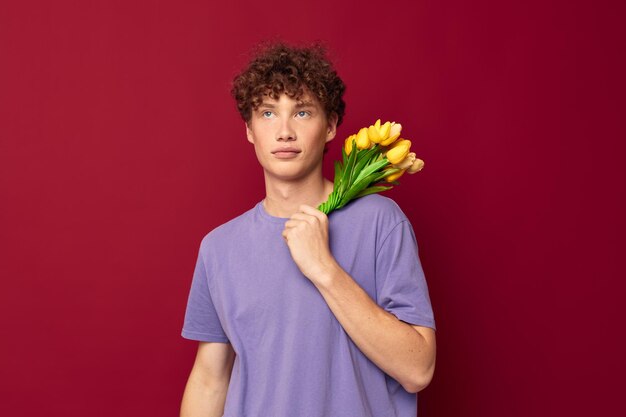 Chico joven sosteniendo un ramo amarillo de flores camisetas moradas fondo rojo inalterado