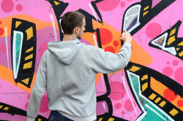 Un chico joven con una sudadera con capucha gris pinta graffiti en rosa y verde