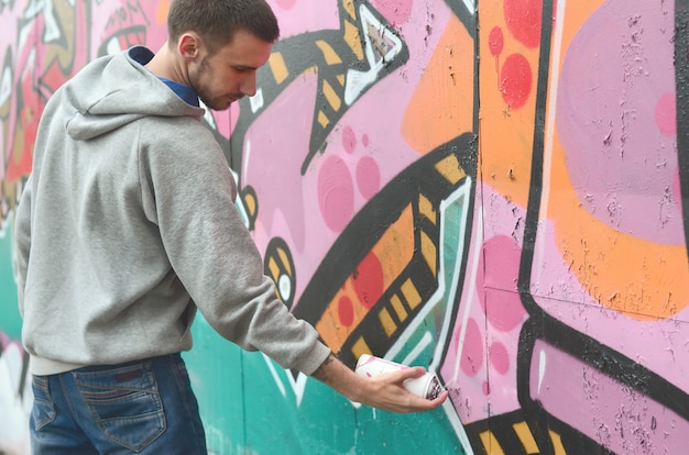 Un chico joven con una sudadera con capucha gris pinta graffiti en rosa y verde