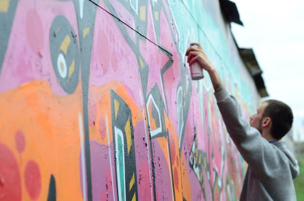 Un chico joven con una sudadera con capucha gris pinta graffiti en rosa y verde