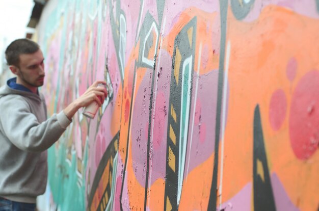 Un chico joven con una sudadera con capucha gris pinta graffiti en rosa y verde