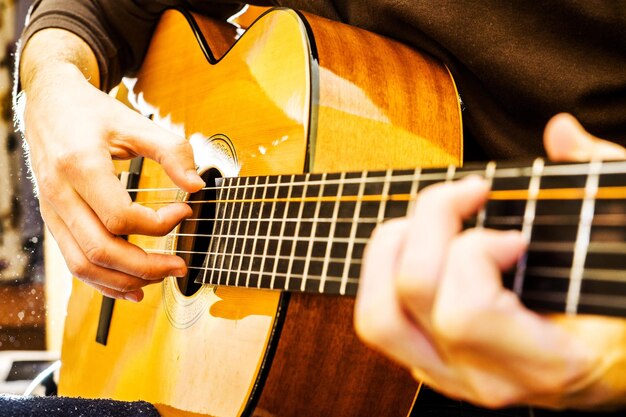 El chico joven tocando una guitarra acústica disparando a contraluz