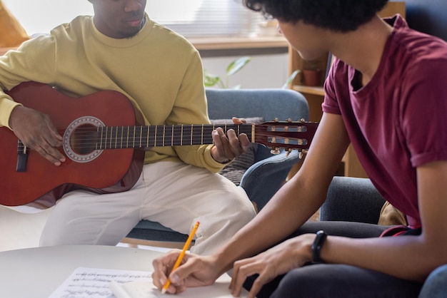 Chico joven tomando notas y mirando al profesor de música tocando la guitarra