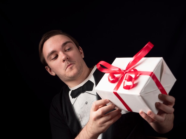 Un chico joven con un traje de camiseta negra sostiene con sorpresa un regalo en un negro