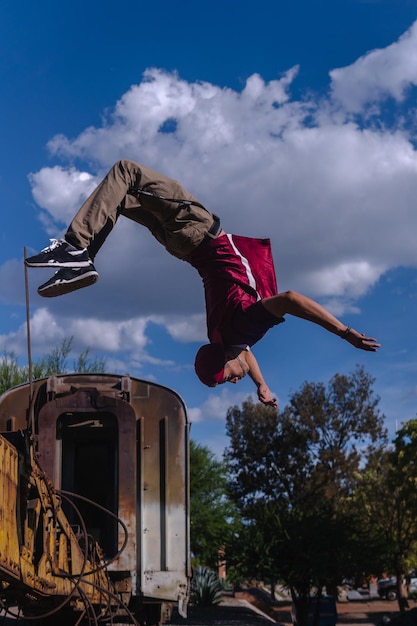 Foto chico latino haciendo una voltereta lateral en un tren abandonado hombre hispano practicando parkour