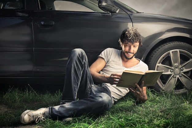Chico leyendo un libro al lado de su auto