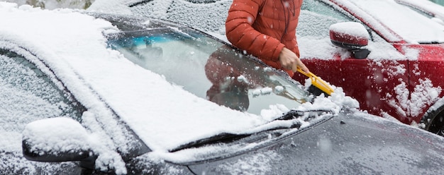 El chico limpia el coche de la nieve con un cepillo, concepto de mal tiempo en la nieve