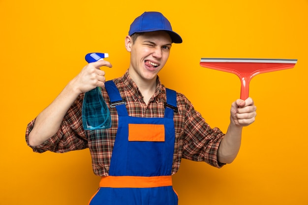 Chico de limpieza joven con uniforme y gorra con agente de limpieza con cabeza de trapeador aislado en la pared naranja