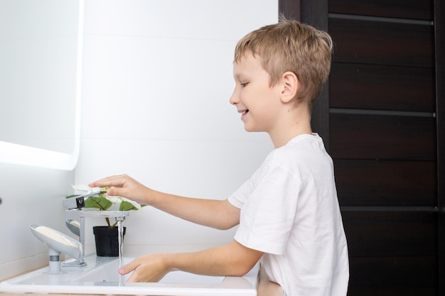 Chico lindo abre el agua para lavarse las manos y lavarse sonriendo