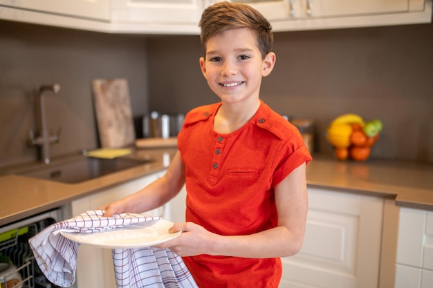 Chico lindo alegre secando un plato limpio con una toalla