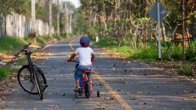 Un chico lindo andando en bicicleta cerca de la bicicleta grande de su padre.