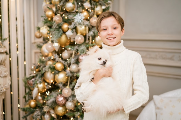 Chico lindo en el árbol de navidad con perro en previsión de feliz navidad niño feliz y perro abraza a su te ...