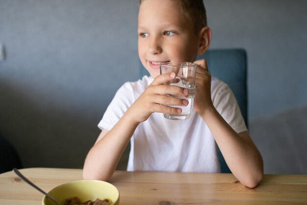 Un chico lindo bebe agua y come un desayuno seco en casa y sonríe.