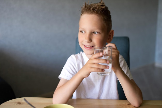 Un chico lindo bebe agua y come un desayuno seco en casa y sonríe.