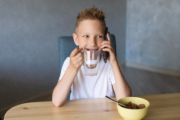 Un chico lindo bebe agua y habla por teléfono Desayuno