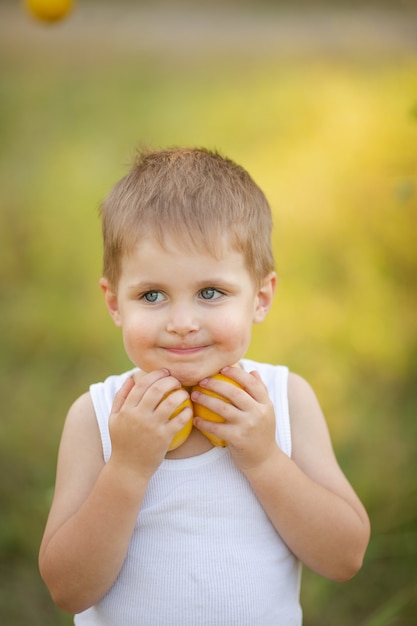 Un chico lindo con cabello rubio con una camiseta blanca con limones de verano en el jardín debajo de un árbol
